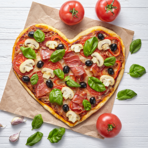 Heart shaped pizza surrounded by tomatoes and basil 