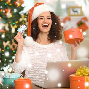 Woman with a gift card in one hand and a present in the other wearing a Santa hat shopping online