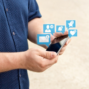 A man wearing blue shirt holding cell phone with social media icon bubbles sprouting from it
