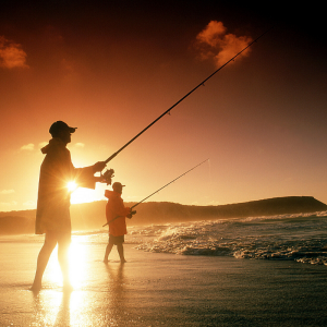 Two men fishing on the beach at sunset