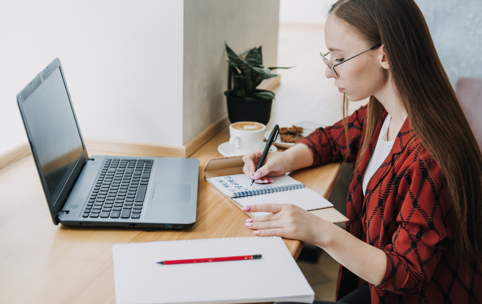 Person researching on the computer and writing down their goals