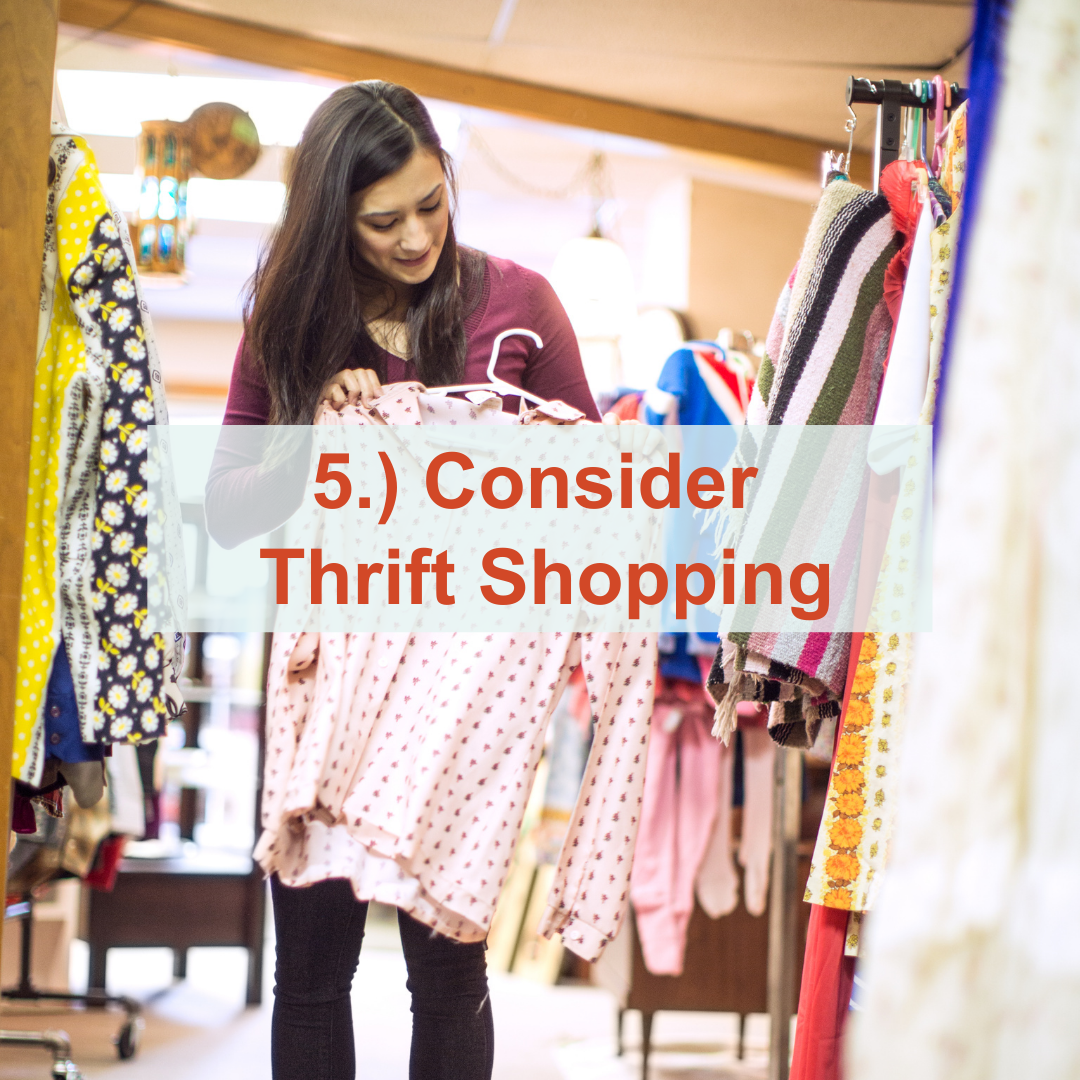 Woman holding a shirt up next to a rack of clothes | Consider Thrift Shopping