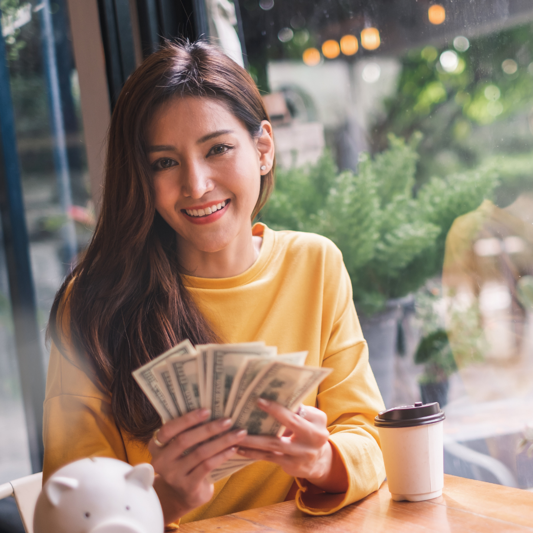 A woman with long brown hair holding a stack of cash sitting at a restaurant table