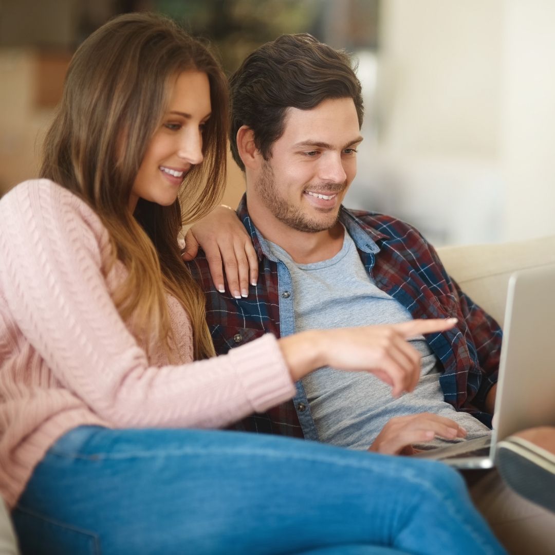 a man and woman sitting on a couch looking at laptop